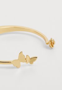Gold-tone metal cuff bracelet featuring two butterfly accents and a rose detail on one end. Smooth finish with a polished look.