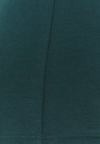 Mørkegrønt stof med en glat tekstur, der har et sømløst design og subtile syninger langs kanterne. Ingen synlige mønstre.