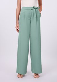 Light green wide-leg trousers with a fabric tie belt, pleated front, and side pockets. Smooth texture and full-length design.