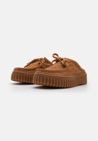 Suede brown slip-on shoes with a chunky, textured rubber sole and stitched detailing. Laces tied at the front with a smooth finish.