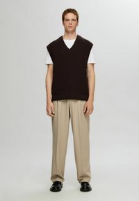 Dark brown knitted sleeveless vest with a v-neck, worn over a white t-shirt, paired with beige trousers and black shoes.