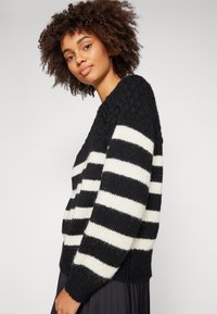 Mustriline mustvalge kootud jumpers, mis on chunky kootud tekstuuriga, langetatud õlgade ja soonikuga hemiga. soe ja mugav materjal, mis sobib ideaalselt kihistamiseks.