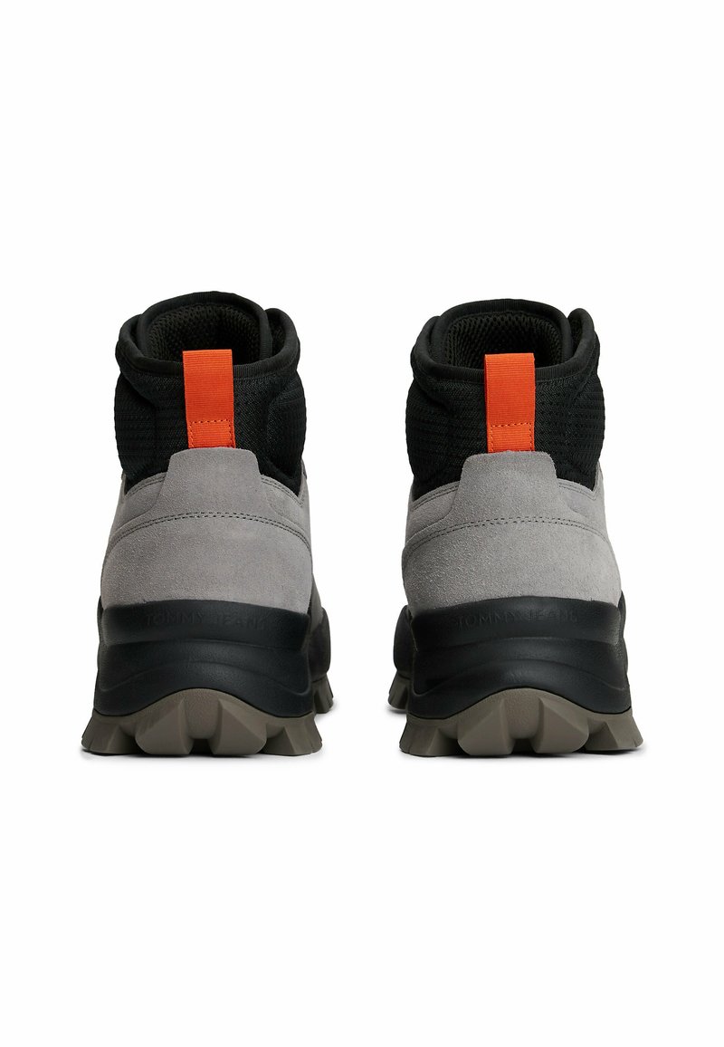 Graue Wildleder- und schwarze Mesh-Stiefeletten mit einem orangefarbenen Zuglasche, ausgestattet mit einer klobigen schwarzen Außensohle und strukturiertem Gummi für besseren Halt.