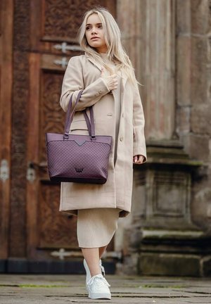 Purple quilted tote bag with dual handles and accent detailing. Worn with a beige coat and knit dress, paired with white sneakers.