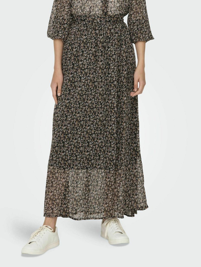 Lungo abito maxi nero con stampa floreale, vita stretta, tessuto trasparente e maniche tre quarti, abbinato a sneaker bianche.