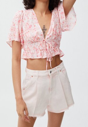 Blouse courte rose à motif floral avec un col en V et une taille à cordon ; associée à un short en denim rose clair taille haute avec des bords effilochés.