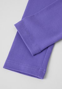 Paarse katoenen stof met een gladde textuur en zichtbare stikdetails. Bevat omgevouwen randen en een nette afwerking aan de mouwen.