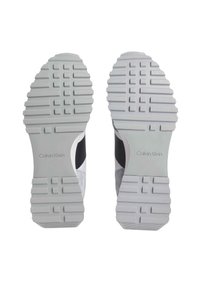 Zapatillas blancas con una suela de goma texturizada, que presentan un diseño moldeado, acentos en gris y negro, y el logo de Calvin Klein en el talón.