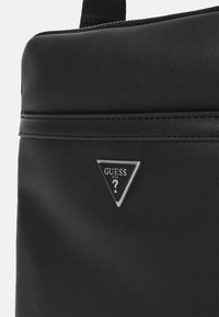 Borsa a mano nera in materiale sintetico con una superficie testurizzata, un accentuato logo triangolare in argento e dettagli cuciti lungo i bordi.