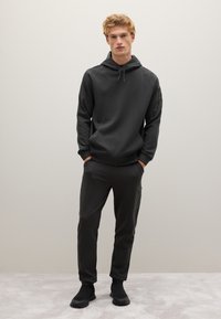 Dunkelgrauer Hoodie mit Kordelzug, Raglanärmeln und Seitentaschen, kombiniert mit passenden, schmal geschnittenen Jogginghosen mit strukturierten Patches.