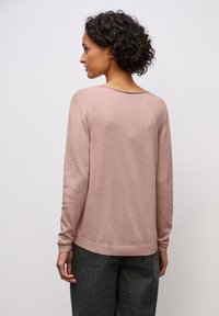 Hellrosa Pullover mit gerippten Bündchen an Ärmel und Saum. Glatte Textur, lockere Passform und weiter Ausschnitt, kombiniert mit dunkelgrauer Hose.