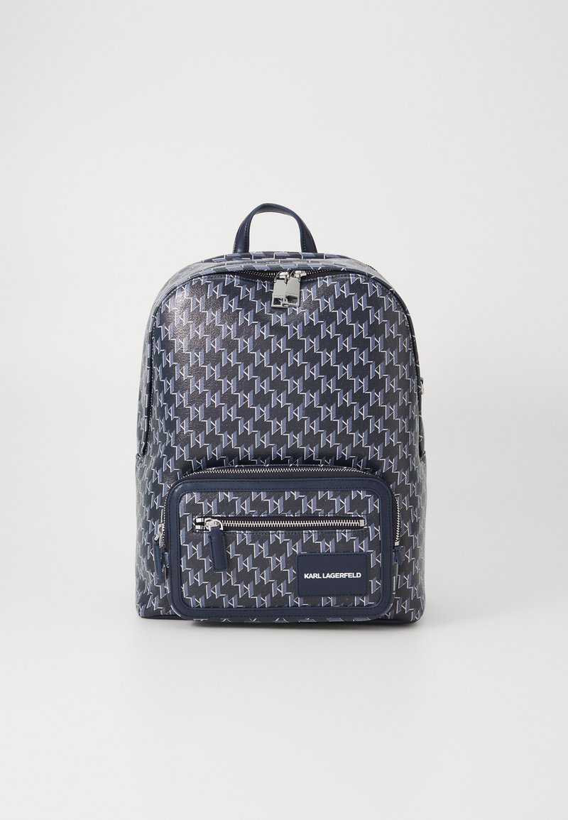 Mochila azul marinho com um padrão geométrico, material suave, bolso frontal com fecho, pega superior e detalhe do logotipo na parte da frente.