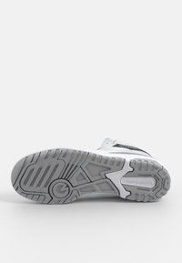 White athletic shoe with a textured rubber sole. Features black accents, a cushioned upper, and a logo on the side, designed for comfort.