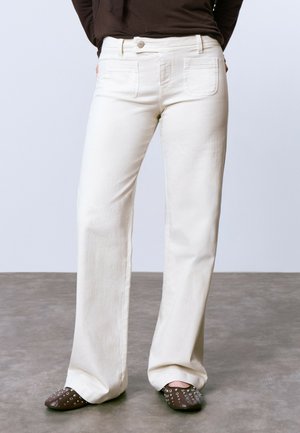Jeans de pierna ancha color crema con bolsillos frontales y traseros, que cuentan con un cierre de botón y una textura suave. Combinando con mule marrones con tachuelas.