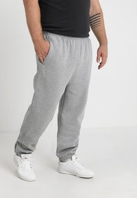 Pantalones de chándal grises hechos de una tela suave, con cinturilla y puños elásticos, que incluyen bolsillos laterales y un corte relajado. Llevados con zapatillas blancas.