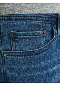 Jeans de mezclilla azul con una textura desgastada, que presentan un pequeño bolsillo trasero con remaches de metal negro y costura en contraste a lo largo de las costuras.
