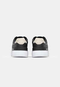 Baskets en cuir noir et beige avec une texture lisse, semelles en caoutchouc blanches et un logo sur le talon. Conçues avec un bout rond et un col rembourré.