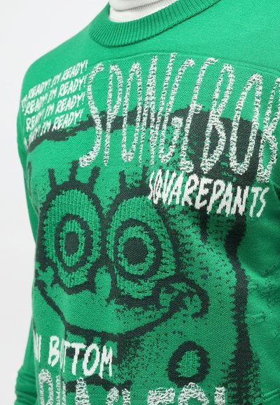 Zeleno pulover s potiskom Spongeboba Pantočnika. Grafika vključuje velike oči in besedilo "SOVRAŽIM!" v belem, z strukturiranim pletenim materialom.