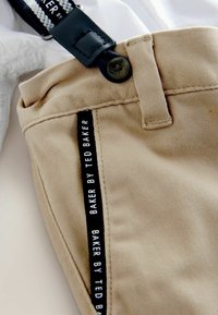 Bežiniai kelnių išlyginta tekstūra, su juodu ženklu "BAKER BY TED BAKER" ir tamsiai mėlynomis detalėmis.