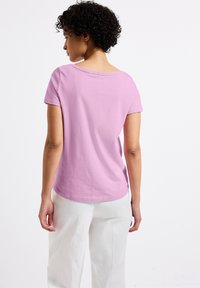 T-shirt rose clair à manches courtes avec un col rond, texture douce et coupe décontractée, associé à un pantalon blanc ample.