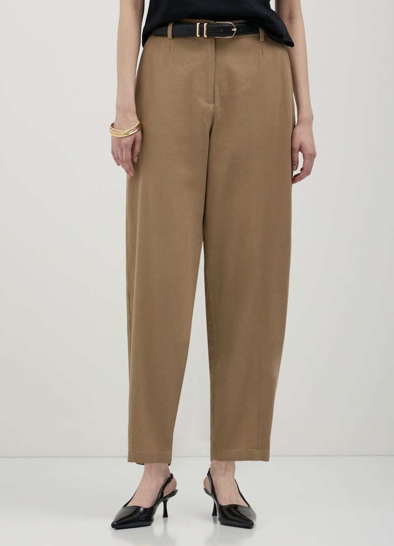Pantalon large couleur beige en tissu léger, avec un pli avant classique et des poches latérales, associé à une ceinture noire.