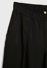 Schwarze, weit geschnittene Hose mit elastischem Bund, seitlichen Taschen und glattem, leichtem Stoff. Minimalistisches Design, keine sichtbaren Muster.