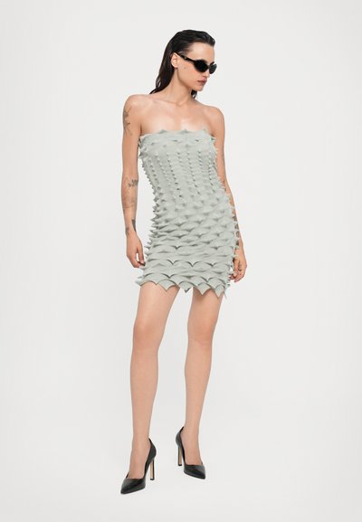 Vestido corto sin tirantes en verde claro con un diseño texturizado y espinoso. Presenta un dobladillo festoneado y se combina con zapatos de tacón negros.