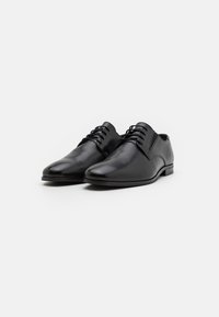 Chaussures habillées en cuir noir avec une texture lisse, bout arrondi, design à lacets et un talon bas et plat. Silhouette propre et minimaliste.