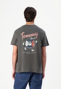 Tmavě šedé bavlněné tričko s barevnou grafikou vinylové desky na zadní straně a textem "Tommy Jeans", klasický kulatý výstřih a krátké rukávy.