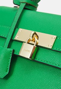Green textured synthetic handbag with gold metal hardware, featuring a padlock closure and a flat strap above a smooth panel.