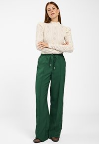 Crèmekleurige gebreide trui met diamanten patroon, gecombineerd met donkergroene wijde broek met zijstrepen en een trekkoord in de taille.