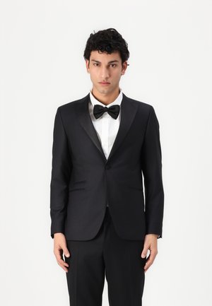 Black tuxedo with satin peak lapels, single button closure, and side pockets; paired with a white dress shirt and black bow tie.