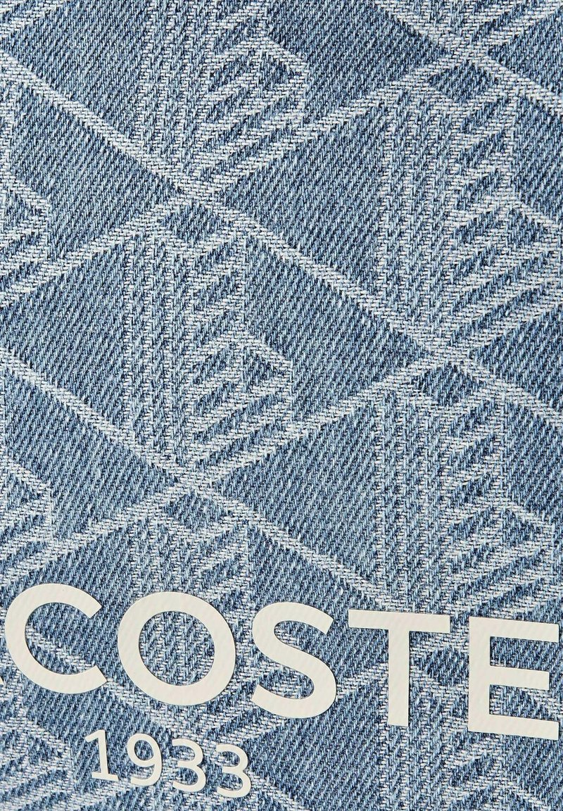 Tessuto di denim blu con motivo a corona bianca ripetuto e testo bianco "COSTE" e anno "1933" stampati su di esso.