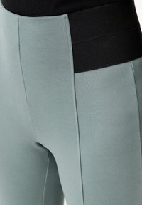 Leggings sportivi verde menta con fascia nera in vita, caratterizzati da una texture liscia e dettagli cuciti lungo i lati.