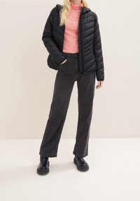 Černá nadýchaná bunda s kapucí, prošívaný design; světle růžový rolák; tmavě šedé široké džíny; černé robustní boty.
