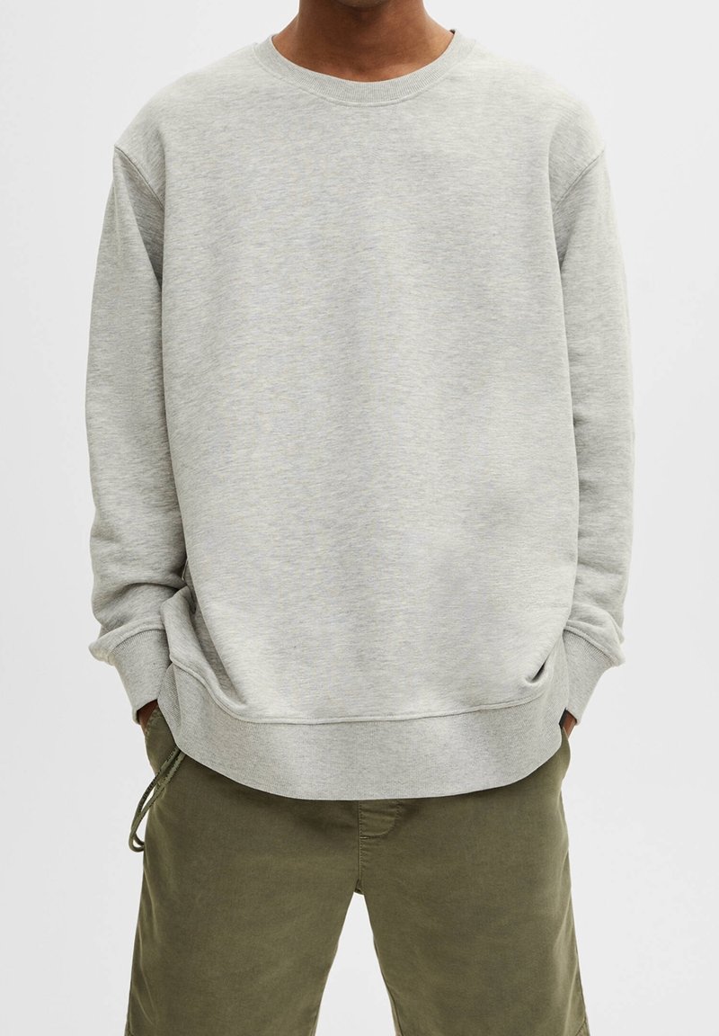 Sudadera gris claro con cuello redondo, hombros caídos y puños acanalados. Tiene un corte holgado y una tela suave y texturizada.