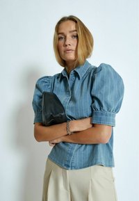 Jeansskjorta med puffärmar och vertikala vita ränder, tillsammans med en svart kuvertväska och ett silverarmband. Ljust beige byxor.