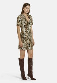Leopardenmusterkleid in Creme und Braun, mit kurzen Ärmeln, figurbetontem Design. Braune Stiefel bis zum Knie mit spitzer Zehenform und Krokodillederoptik.