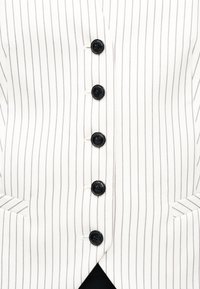 Λευκό ένδυμα με λεπτές κάθετες μαύρες ρίγες, πέντε μαύρα κουμπιά στο κέντρο και δύο μικρές εμπρόσθιες τσέπες.
