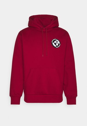 Sweatshirt à capuche rouge en tissu doux, avec une poche avant, des cordons de serrage et un logo brodé circulaire sur la poitrine.