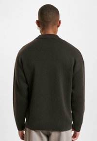 Donkergroene gebreide trui met een hoge kraag, ingezakte schouders en geribbelde manchetten. Zachte textuur met een oversized pasvorm.