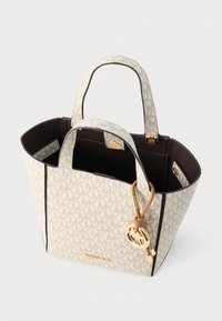 Tote bag en toile blanche avec un motif monogramme, intérieur marron, double poignées supérieures, ferrures dorées et un porte-bijou amovible.