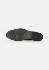Suola di una scarpa marrone scuro con modelli di presa testurizzati e nome del marchio "bugatti" impresso sulle aree del tallone e dell'arco.