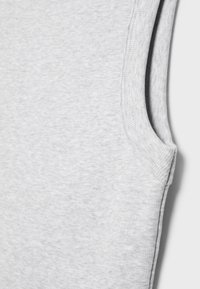 Nahaufnahme eines grauen ärmellosen Baumwollshirts, das die Stoffstruktur und Detailnähte an der Armausschnittkante vor weißem Hintergrund zeigt.