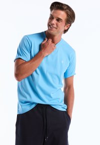 T-shirt en coton bleu clair à manches courtes et col rond, arborant un petit logo de pingouin blanc sur la poitrine gauche.