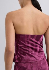 Top sin tirantes en magenta profundo con una superficie texturizada y brillante, que presenta líneas verticales. El diseño incluye un corsé ajustado y un dobladillo recto.
