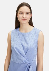 Hellblaues Kleid mit einem strukturierten Blumenmuster, Rundhalsausschnitt und einer verdrehten Knotendetail an der Taille. Ärmelloses Design.