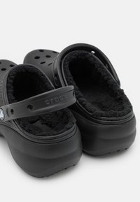 Sabots Crocs noirs avec une doublure douce et moelleuse, des côtés perforés et une sangle. Tige texturée et forme arrondie, conçus pour le confort et la facilité.