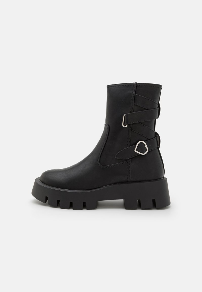 Bottine en cuir noir avec semelle crantée épaisse, brides latérales et détail boucle métallique en forme de cœur.