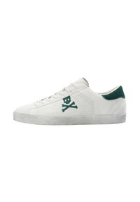 Zapatilla de ante blanca con un tabique de talón de ante verde, que presenta un logo de calavera y huesos cruzados verde en el costado y una suela de goma texturizada gris.